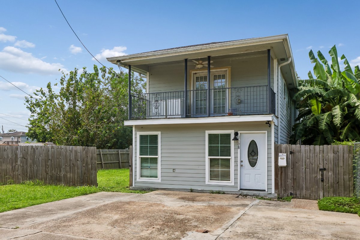 2308 Delery Street, a two-story light gray home with a second-floor balcony and wood privacy fence in the Lower Ninth Ward of New Orleans