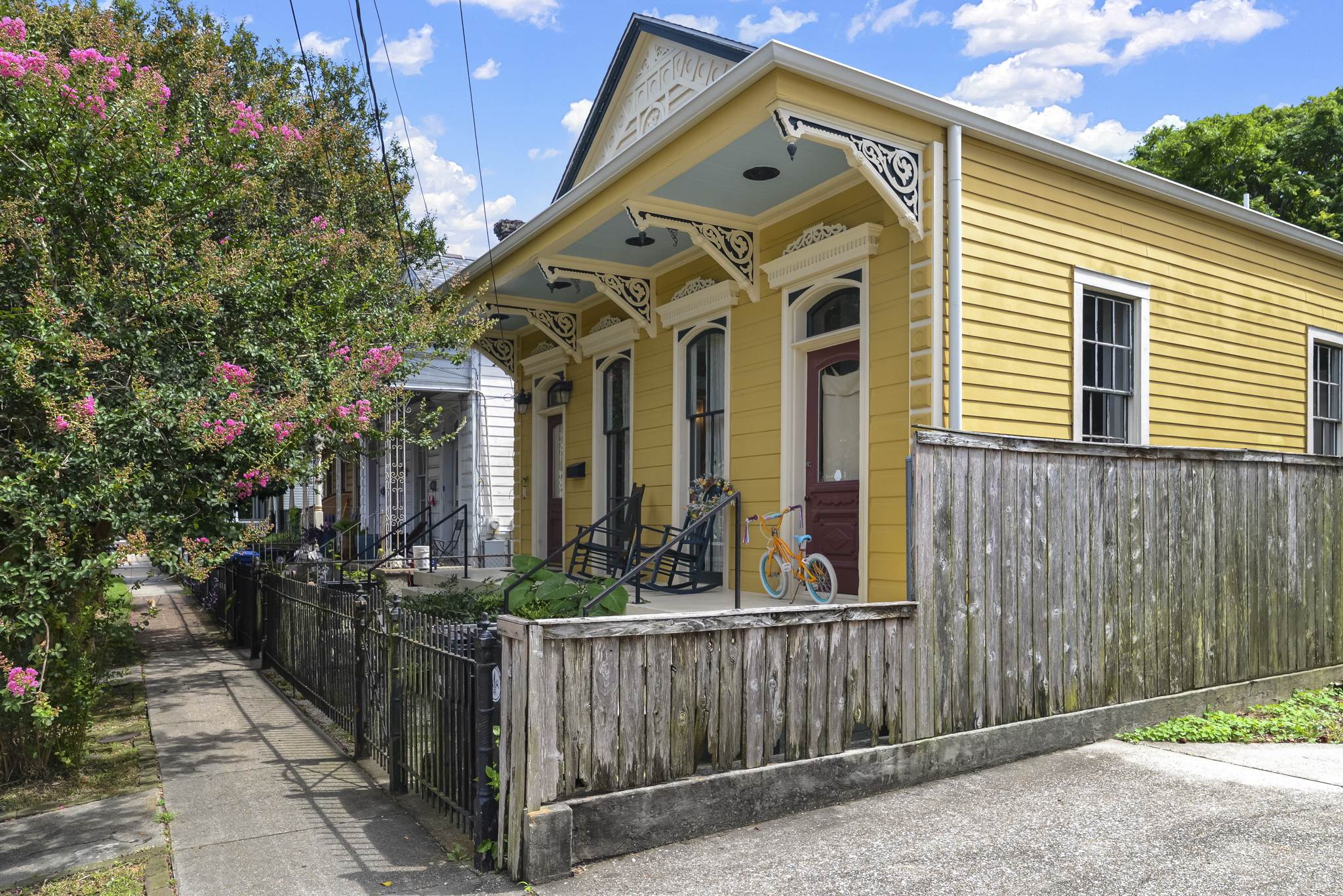 Yellow Victorian cottage with gingerbread trim along a tree-lined Irish Channel street in New Orleans