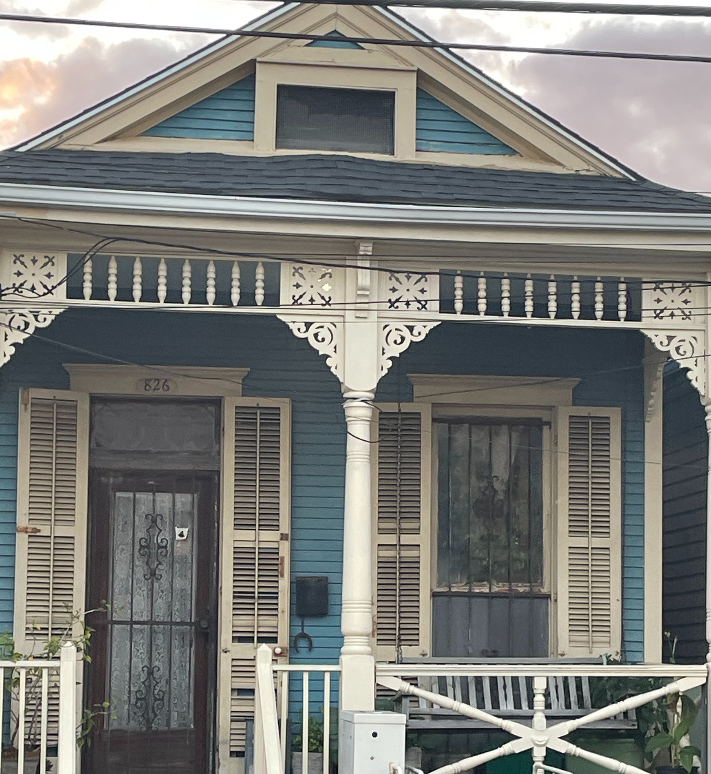 Blue Victorian shotgun cottage with white gingerbread millwork and turned porch columns in the Leonidas neighborhood of New Orleans